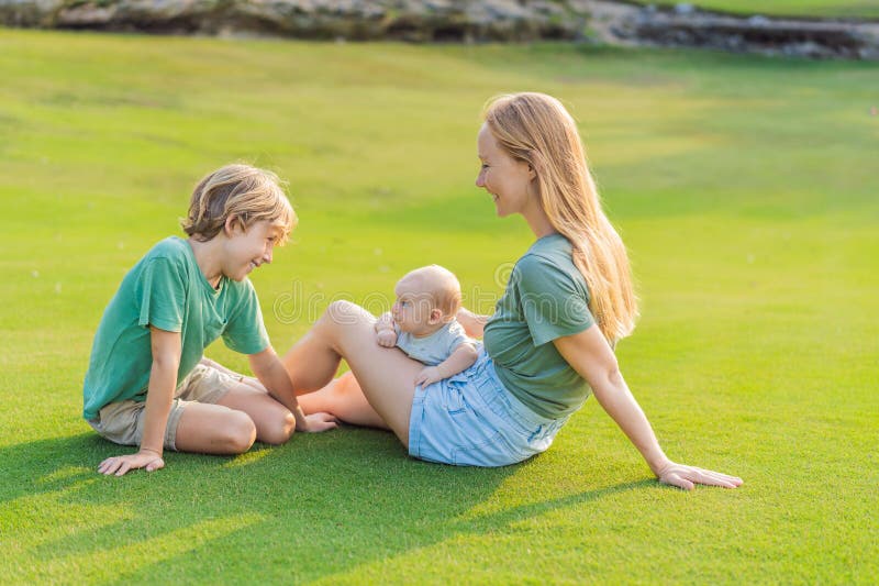 Moderäldre son och nyfödda barn på en ängsmark i parken. Familjeutgifter av hög kvalitet tillsammans i naturen. Parenthood fotografering för bildbyråer