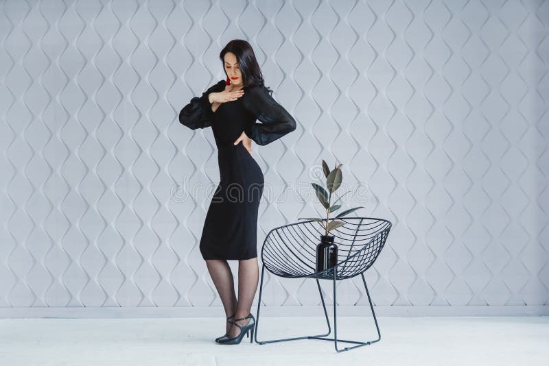 Modestående av en stilfull brunettflicka som bär en svart klänning Kvinna med långt hår som bär röda örhängen modell royaltyfri fotografi Modestående av en stilfull brunettflicka som bär en svart klänning Kvinna med långt hår som bär röda örhängen modell royaltyfri fotografi