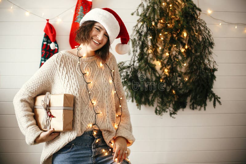 Modieus gelukkig meisje in van de holdingskerstmis van de santahoed de giftdoos op achtergrond van moderne Kerstmisboom, lichten royalty-vrije stock foto's Modieus gelukkig meisje in van de holdingskerstmis van de santahoed de giftdoos op achtergrond van moderne Kerstmisboom, lichten royalty-vrije stock foto's