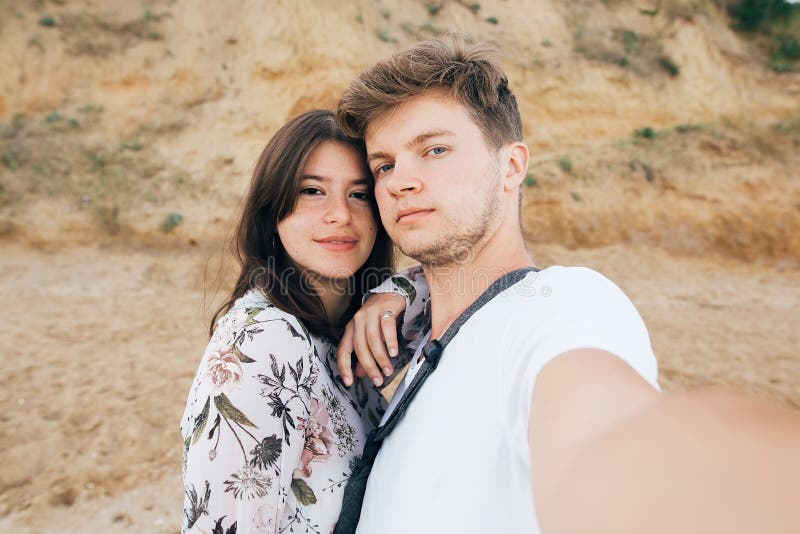 Modieus hipsterpaar die selfie op strand bij zandige klip op zee nemen De vakantie van de zomer Portret van gelukkige jonge famil stock afbeelding Modieus hipsterpaar die selfie op strand bij zandige klip op zee nemen De vakantie van de zomer Portret van gelukkige jonge famil stock afbeelding