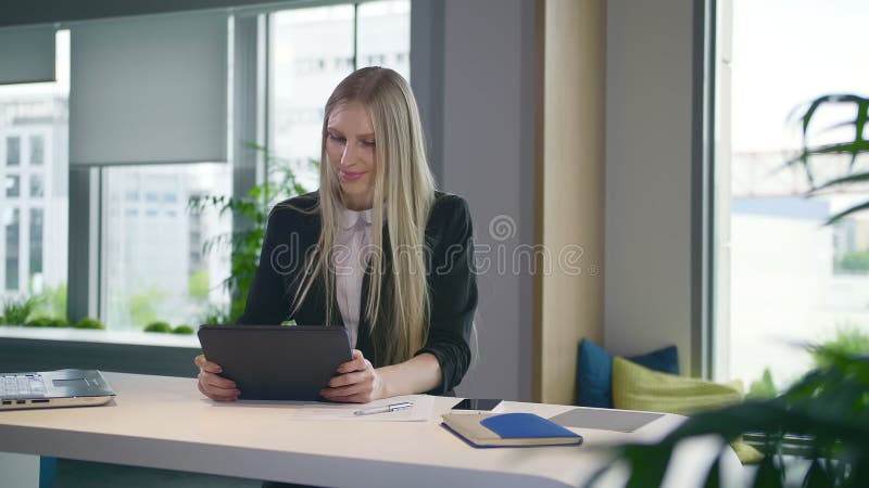 Modieuze bedrijfsvrouw met tablet in bureau Elegante vrouw in kostuumzitting bij lijst met binnen laptop en het surfen tablet