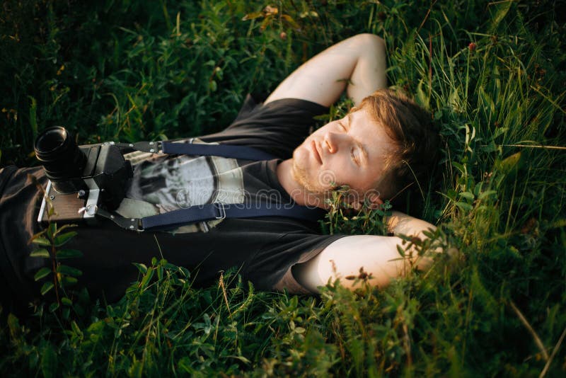 Modieuze hipstermens met de camera die van de filmfoto in groen gras liggen en in zonnige weide bij atmosferische zonsondergang o royalty-vrije stock fotografie Modieuze hipstermens met de camera die van de filmfoto in groen gras liggen en in zonnige weide bij atmosferische zonsondergang o royalty-vrije stock fotografie