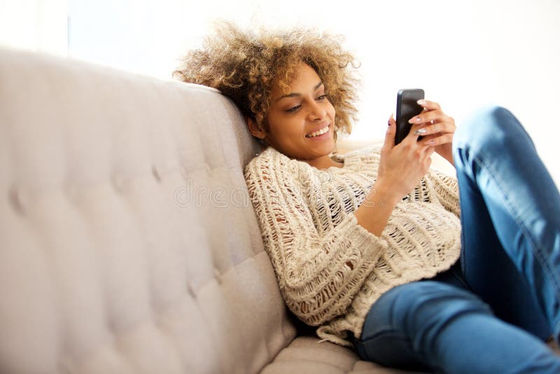 Modische junge Frau, die zu Hause sitzt und Mobiltelefon betrachtet lizenzfreie stockfotos Modische junge Frau, die zu Hause sitzt und Mobiltelefon betrachtet lizenzfreie stockfotos
