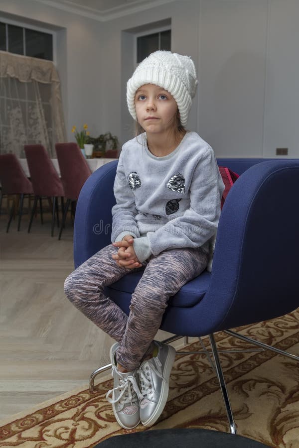 fashionable girl in white knitted hat and warm sweater is sitting in chair and watching cartoon on TV. fashionable girl in white knitted hat and warm sweater is sitting in chair and watching cartoon on TV.