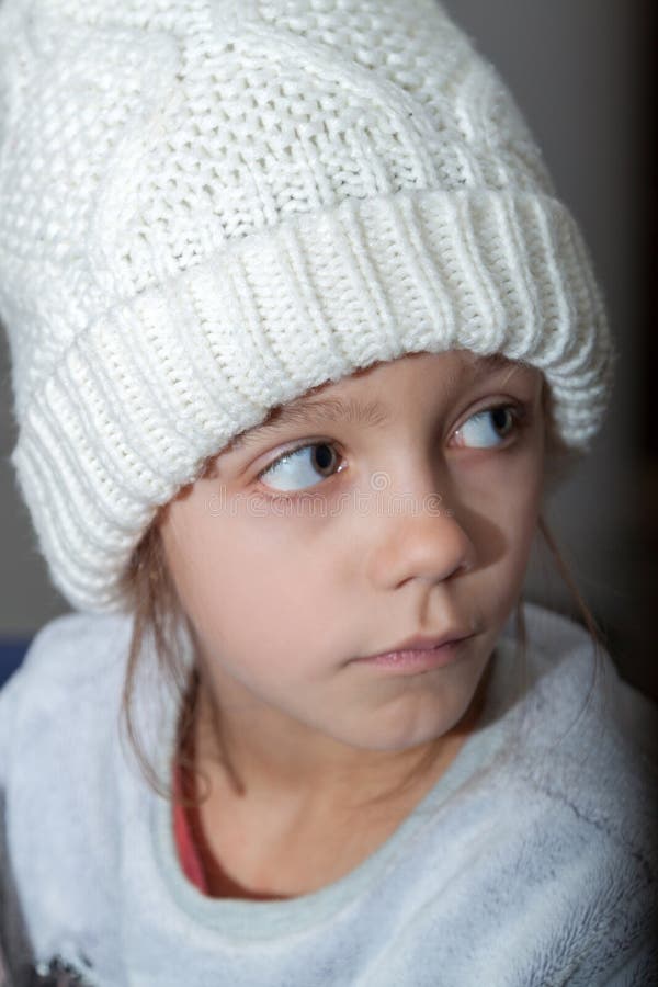 Fashionable girl in white knitted hat and warm sweater is sitting in chair and watching cartoon on TV. Fashionable girl in white knitted hat and warm sweater is sitting in chair and watching cartoon on TV.