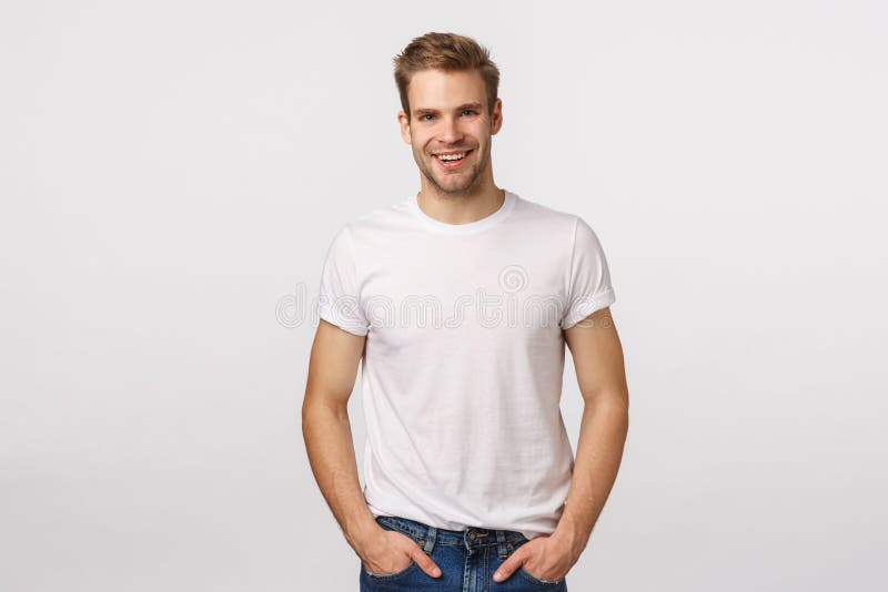Modèle masculin blonde charmant et mature avec des poils, T-shirt blanc d'usure, mains dans les poches, sourire amusé, sembler am