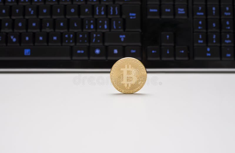 Moeda de Golen Bitcoin que está em uma mesa branca e na frente de um teclado preto com chaves destacadas imagem de stock royalty free Moeda de Golen Bitcoin que está em uma mesa branca e na frente de um teclado preto com chaves destacadas imagem de stock royalty free