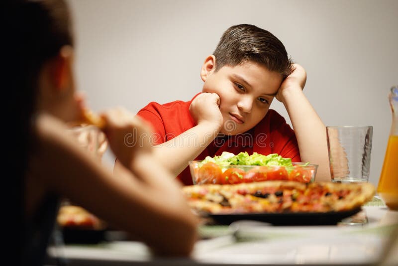 Moeder die Salade in plaats van Pizza geven aan Te zware Zoon stock fotografie Moeder die Salade in plaats van Pizza geven aan Te zware Zoon stock fotografie