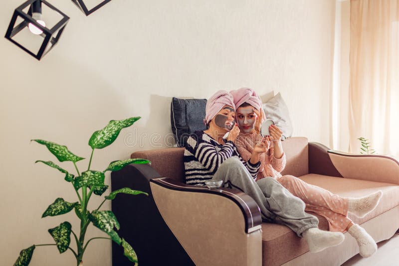 Moeder en haar volwassen dochter die gezichtsmaskers toepassen die spiegel bekijken En vrouwen die thuis koelen ontspannen royalty-vrije stock foto's Moeder en haar volwassen dochter die gezichtsmaskers toepassen die spiegel bekijken En vrouwen die thuis koelen ontspannen royalty-vrije stock foto's