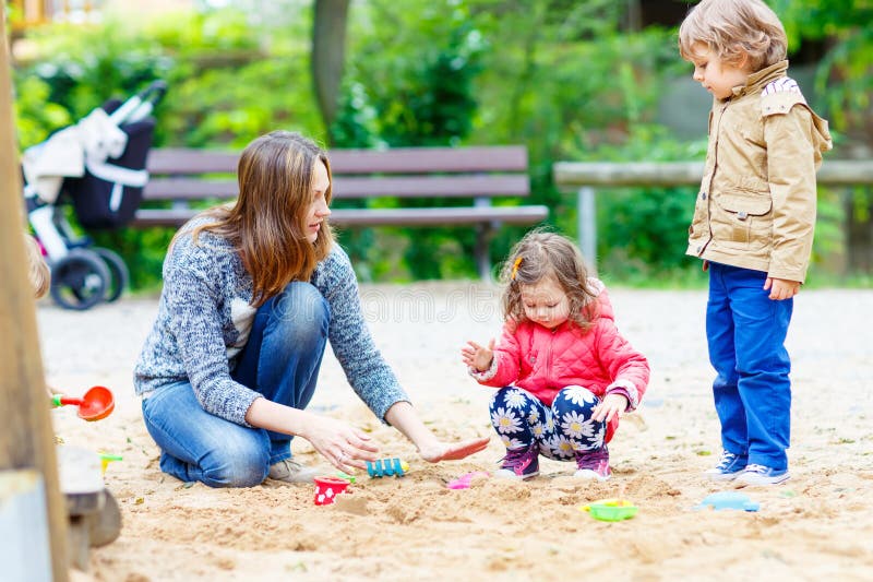 Moeder en twee kleine kinderen die op speelplaats spelen royalty-vrije stock afbeelding Moeder en twee kleine kinderen die op speelplaats spelen royalty-vrije stock afbeelding