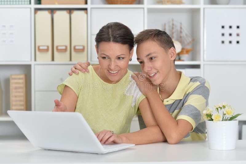 Moeder en zoon die moderne laptop gebruiken aan tafel