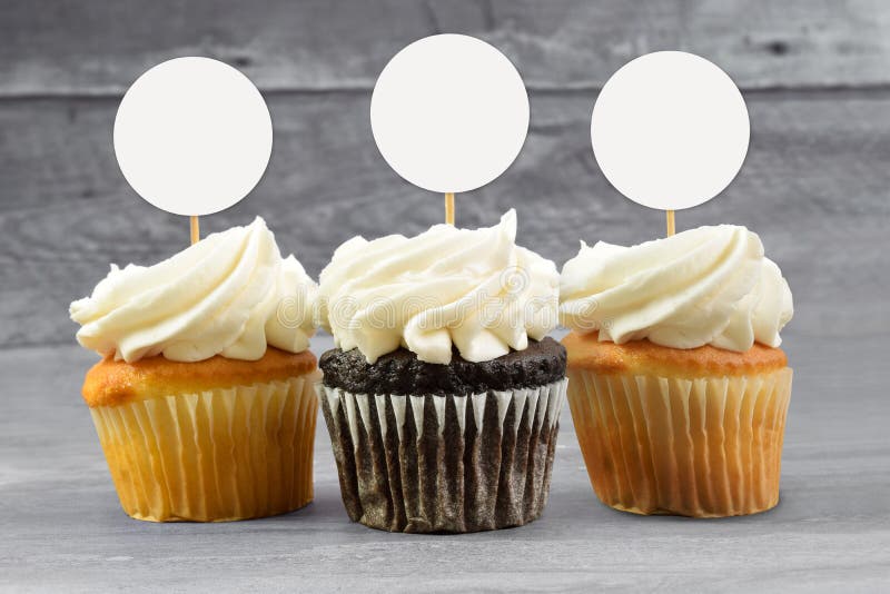 Cupcake topper mockup featuring chocolate and yellow cupcakes sitting temptingly on a gray wooden background. Cupcake topper mockup featuring chocolate and yellow cupcakes sitting temptingly on a gray wooden background