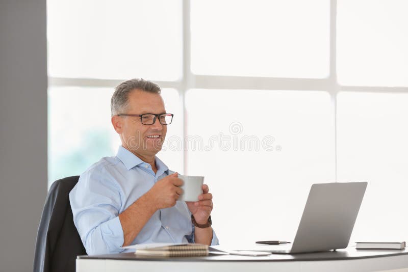 Mogen affärsman som i regeringsställning dricker kaffe på arbetsplatsen arkivbild Mogen affärsman som i regeringsställning dricker kaffe på arbetsplatsen arkivbild