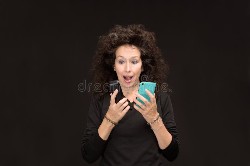Mogen kvinna med den förvånade öppna munnen för 2 mobiltelefoner royaltyfri bild Mogen kvinna med den förvånade öppna munnen för 2 mobiltelefoner royaltyfri bild