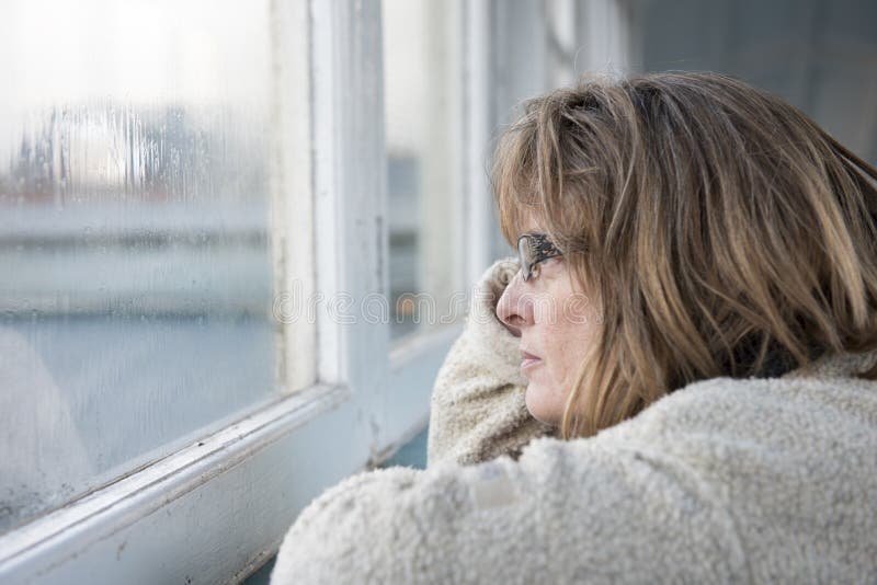Mogen kvinna som ut ser fönstret på en regnig dag arkivbilder