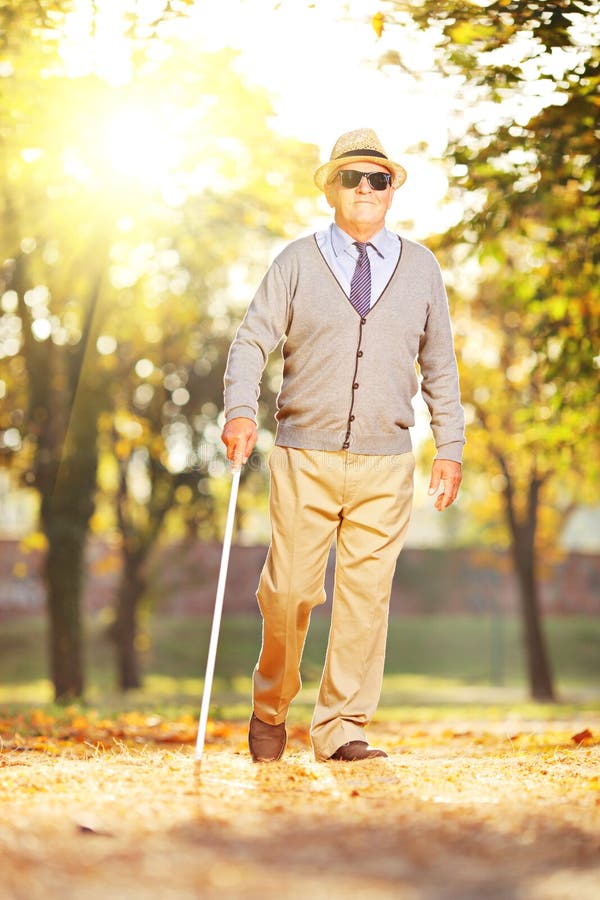 Blind mature man holding a stick and walking in a park on a sunny day. Blind mature man holding a stick and walking in a park on a sunny day