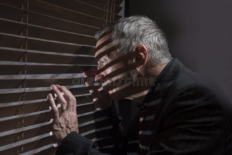 Mogen man som ser ut ur ett fönster med rullgardiner som gjuter skuggor arkivbild