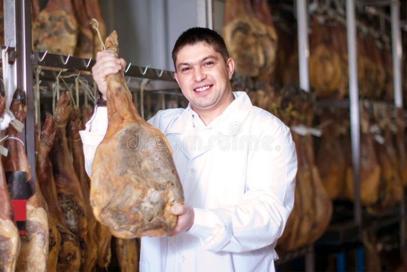 Mogen slaktare som poserar med jamonskarvar på köttfabriken arkivbilder Mogen slaktare som poserar med jamonskarvar på köttfabriken arkivbilder