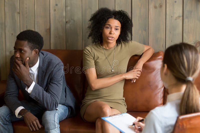 African frustrated wife talking to psychologist sitting on couch with husband, black unhappy women sharing marital problems with counselor, family marriage therapy session, couple counseling concept. African frustrated wife talking to psychologist sitting on couch with husband, black unhappy women sharing marital problems with counselor, family marriage therapy session, couple counseling concept