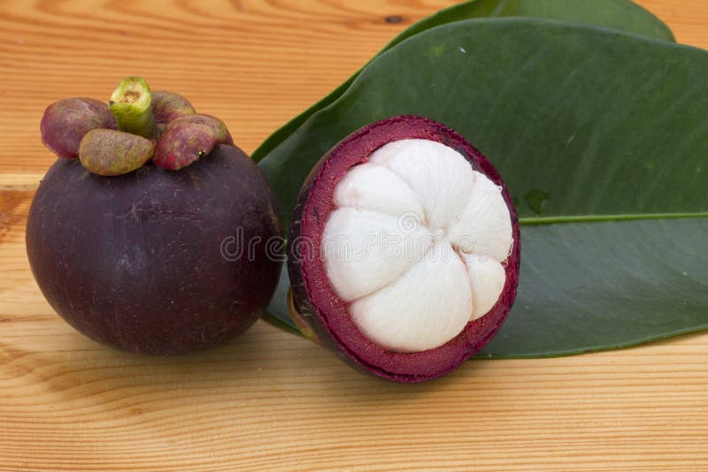 Mogna mangosteens eller halv mangosteen med gröna sidor på en trätabell fotografering för bildbyråer Mogna mangosteens eller halv mangosteen med gröna sidor på en trätabell fotografering för bildbyråer
