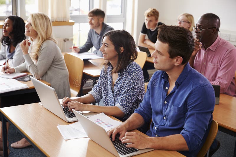 Mogna studenter som sitter på skrivbord i vuxenutbildninggrupp arkivfoto