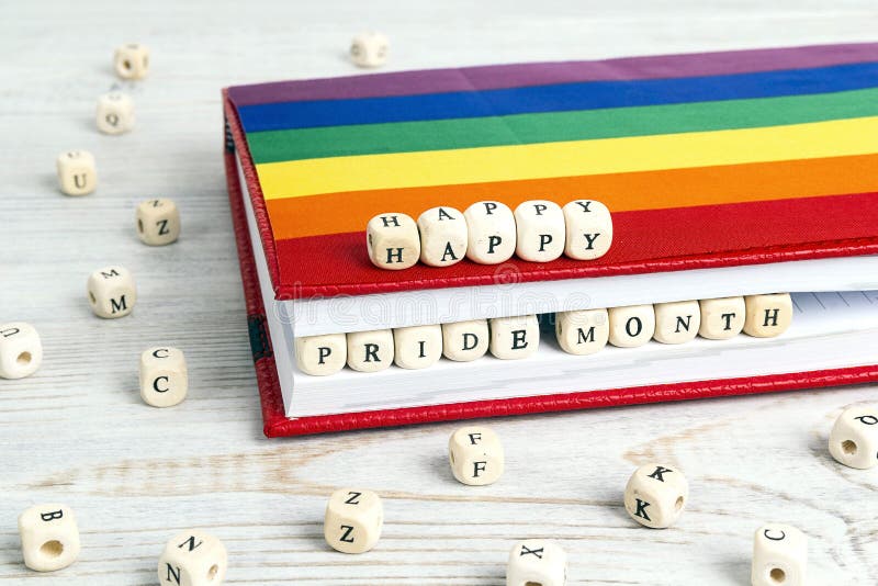 Happy pride month written in wooden blocks in red notebook with rainbow LGBT flag on wooden table. LGBT Pride Month in June. Happy pride month written in wooden blocks in red notebook with rainbow LGBT flag on wooden table. LGBT Pride Month in June