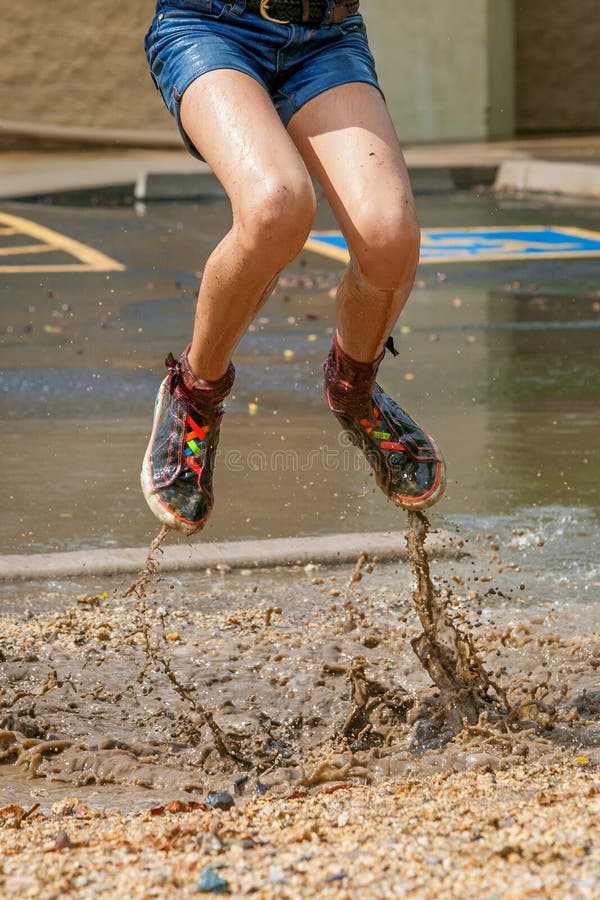 Moitié inférieure d'une fille sautant dans Muddy Puddle image libre de droits Moitié inférieure d'une fille sautant dans Muddy Puddle image libre de droits