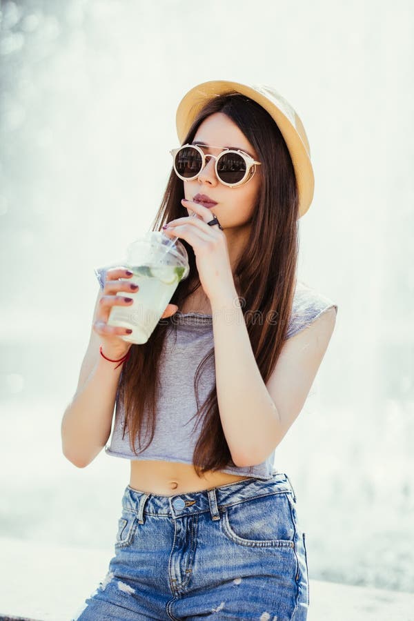 Mojito engraçado positivo de sorriso da bebida do copo da terra arrendada da jovem mulher, luz solar, exterior, estilo da rua per fotografia de stock Mojito engraçado positivo de sorriso da bebida do copo da terra arrendada da jovem mulher, luz solar, exterior, estilo da rua per fotografia de stock
