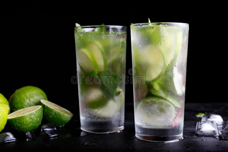 Mojito traditional summer vacation refreshing cocktail alcohol drink in highball glass, soda water beverage, lime juice, mint leaves, sugar, and rum. Dark black background with copy space text