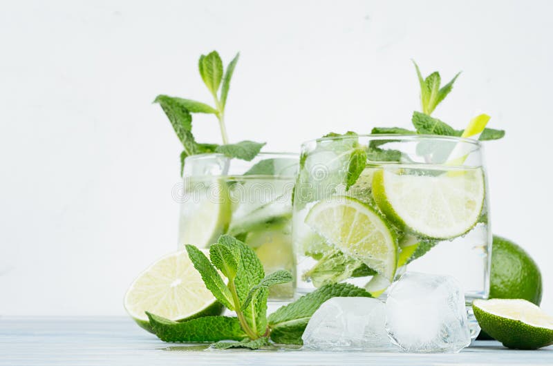 Mojito in two glasses with mint, slices lime, ice cubes, straw on soft white background, copy space.