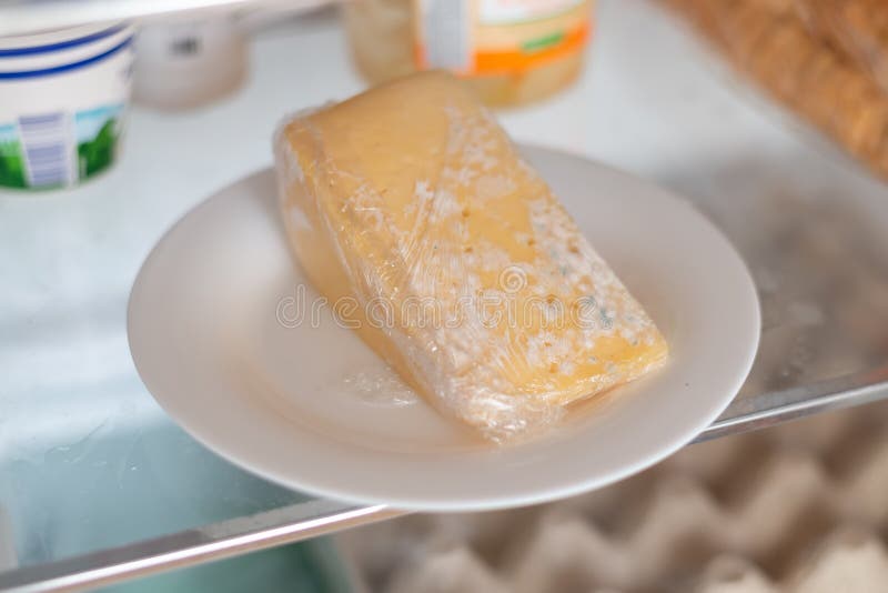 Moldy cheese wrapped in cling film in the refrigerator. Incorrect storage, spoiled product, expired concept.