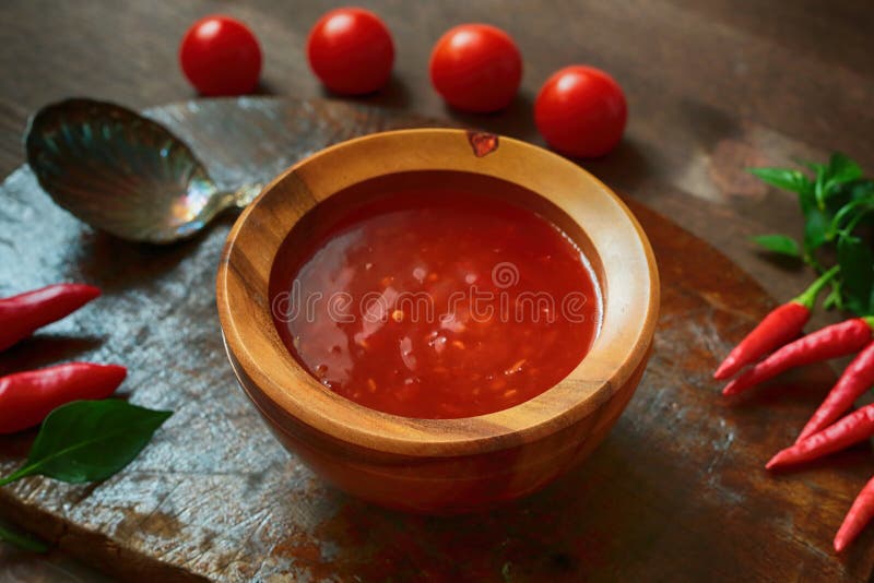 Sweet chili sauce , tomatoes, silver spoon and hot red chili pepper on the brown wooden retro plate. Sweet chili sauce , tomatoes, silver spoon and hot red chili pepper on the brown wooden retro plate