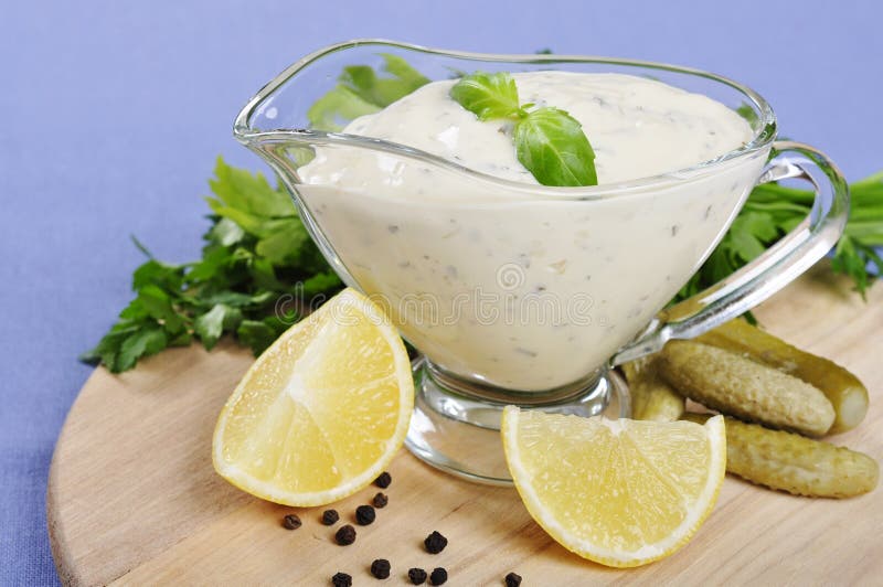 Tartare Sauce in a gravy boat with cucumber and lemon on wooden cutting board. Tartare Sauce in a gravy boat with cucumber and lemon on wooden cutting board