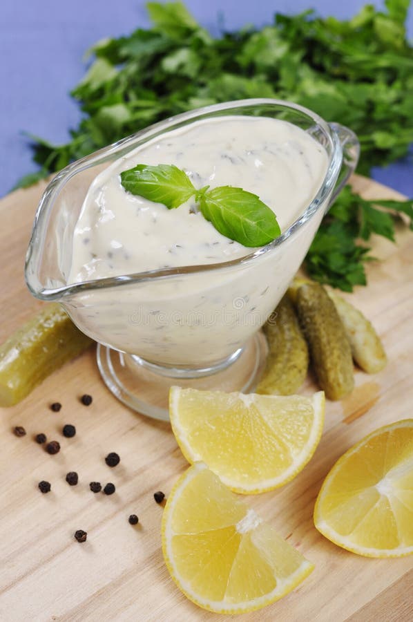 Tartare Sauce in a gravy boat with cucumber and lemon on wooden cutting board. Tartare Sauce in a gravy boat with cucumber and lemon on wooden cutting board