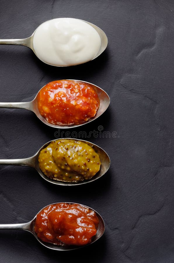 Variety of condiments on vintage spoons on slate background, mayonnaise, tomato sauce, mustard and sweet chilli jam. Variety of condiments on vintage spoons on slate background, mayonnaise, tomato sauce, mustard and sweet chilli jam