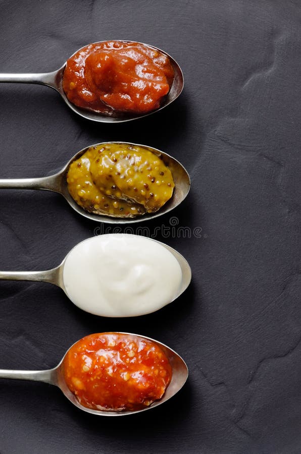 DIfferent types of condiments on vintage spoons on slate background, mayonnaise, tomato sauce, mustard and sweet chilli jam. DIfferent types of condiments on vintage spoons on slate background, mayonnaise, tomato sauce, mustard and sweet chilli jam