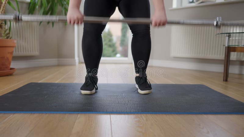 Mollig kaukasisch junge Frau aufziehen Langhantel stehen auf Übungsmatte zu Hause. Beine mit konzentrierter Motivation