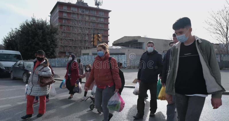 Molti adulti e bambini con maschere coronavirus attraversano la strada dopo che luci verdi e automobili si sono fermate in rosso i