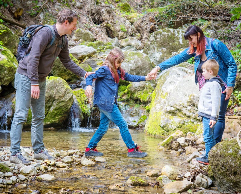 Mom and dad help children cross the mountain stream stock photo