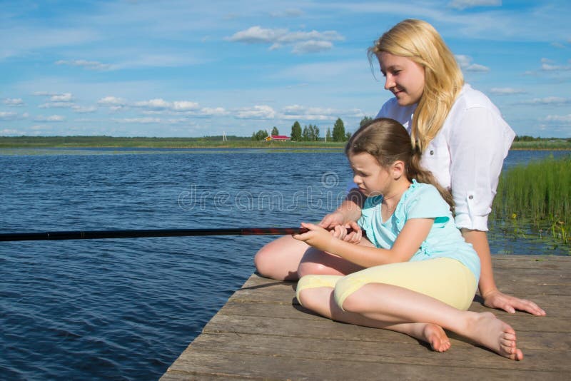 Mom and daughter on the pier, against the backdrop of a beautiful landscape, hold a fishing pole to catch fish, close-up, there is stock photos Mom and daughter on the pier, against the backdrop of a beautiful landscape, hold a fishing pole to catch fish, close-up, there is stock photos