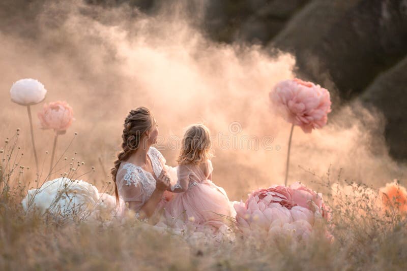 Mom and daughter in pink fabulous dresses look into the distance, sitting in a field surrounded by large pink decorative flowers royalty free stock photos Mom and daughter in pink fabulous dresses look into the distance, sitting in a field surrounded by large pink decorative flowers royalty free stock photos