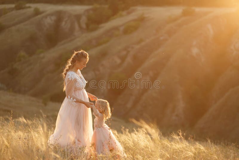Mom with daughter in pink fabulous dresses in nature, holding hands. Sunset sun rays royalty free stock photo Mom with daughter in pink fabulous dresses in nature, holding hands. Sunset sun rays royalty free stock photo