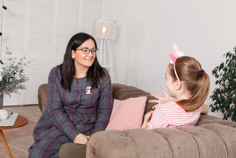 Mom and daughter are sitting on the couch and chatting. Girl teenager with emotions tells her mother a story. Daughter shares her stock photo Mom and daughter are sitting on the couch and chatting. Girl teenager with emotions tells her mother a story. Daughter shares her stock photo