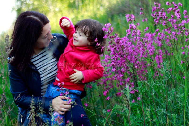 Mom Holds Her Little Curly Daughter In Her Arms In A Flower Meadow 