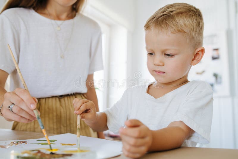 Mom is painting picture with her son on a sheet of paper with acrylic paints