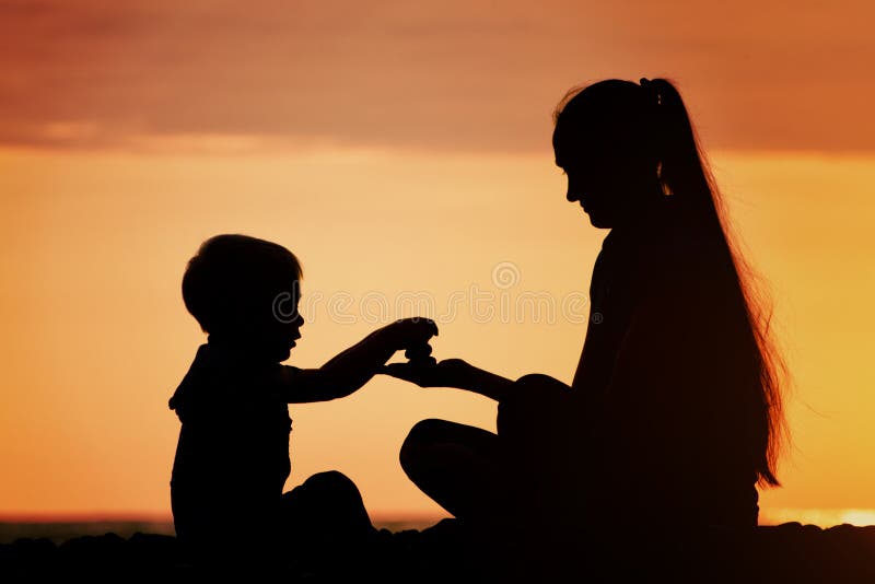 Mom and son playing on the beach with stones. Sunset time, silho stock images Mom and son playing on the beach with stones. Sunset time, silho stock images
