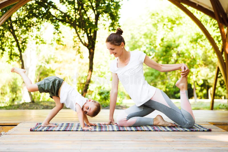 Mom and son are practicing yoga in the park. 