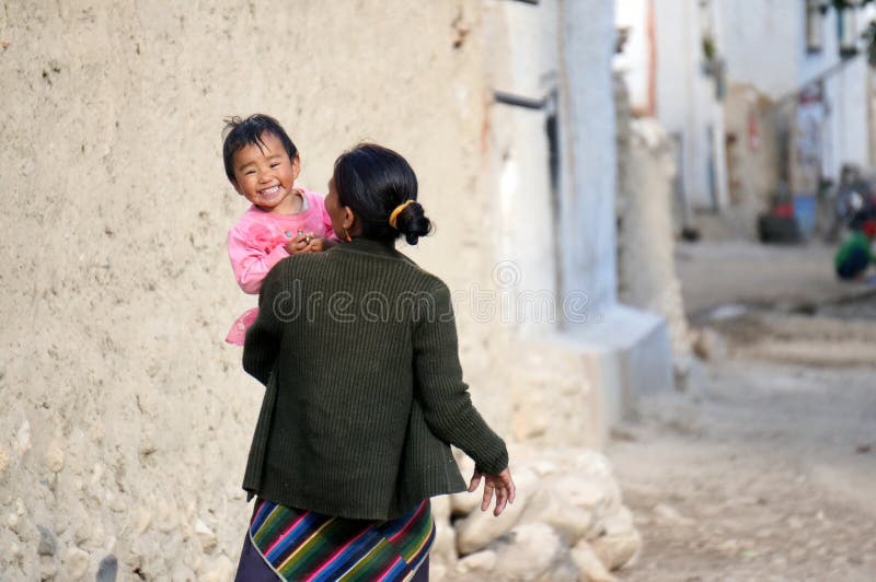 Mom walks along a city street, holding in her arms a small, happy girl in a pink dress