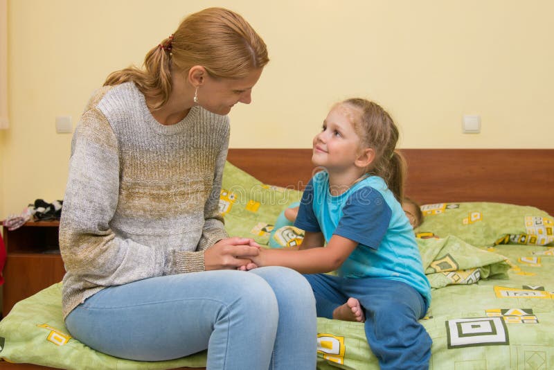 Mom wants to sleep good night to her daughter sitting on the bed in room