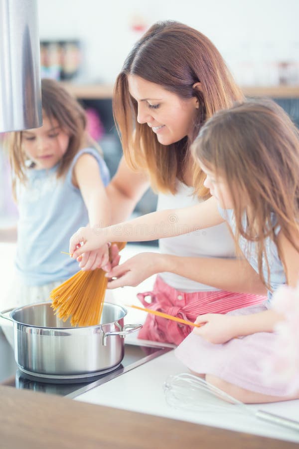 Mom με δύο νέες κόρες διδύμων στα μαγειρεύοντας μακαρόνια κουζινών στοκ φωτογραφία με δικαίωμα ελεύθερης χρήσης Mom με δύο νέες κόρες διδύμων στα μαγειρεύοντας μακαρόνια κουζινών στοκ φωτογραφία με δικαίωμα ελεύθερης χρήσης